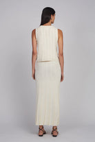 Woman wearing a sleeveless cream top and pleated skirt on a plain background
