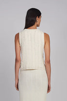 Woman wearing a cream sleeveless top and skirt set on a gray background