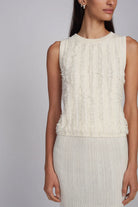 Woman wearing a white sleeveless top with ruffled details on a gray background