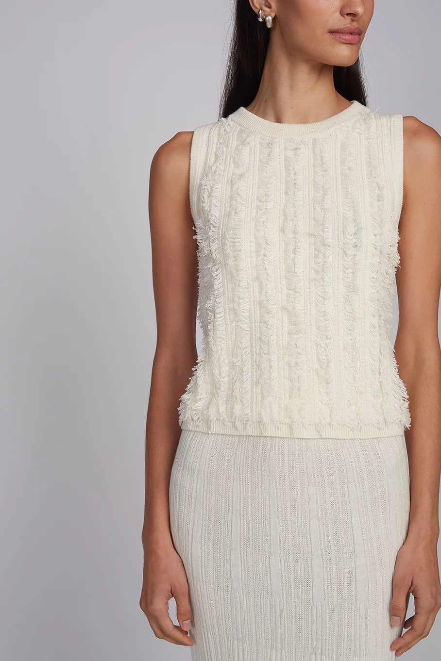 Woman wearing a white sleeveless top with ruffled details on a gray background