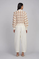 Woman wearing a beige and white patterned top with white pants on a gray background