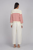 Person wearing a red and white striped sweater with white pants on a plain background
