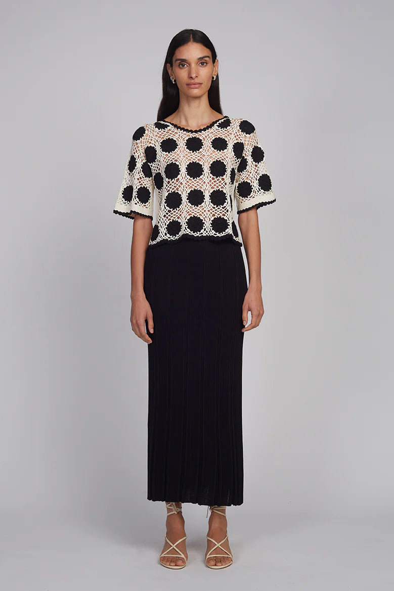 Woman wearing a black and white polka dot top with a long black skirt on a gray background