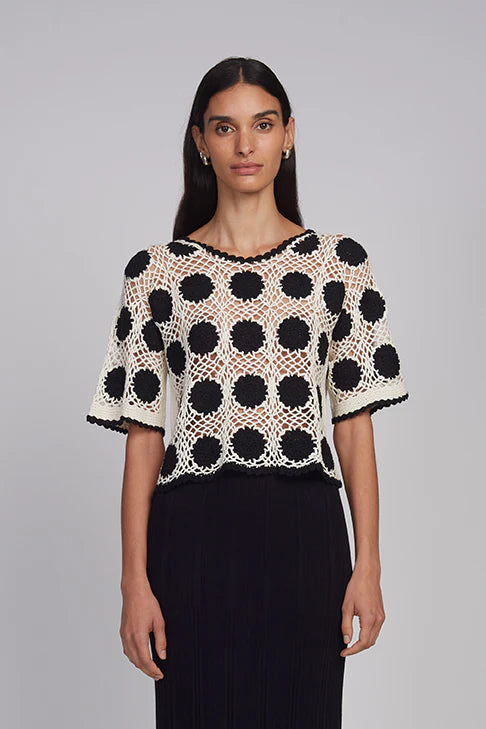 Woman wearing a black and white polka dot top against a gray background