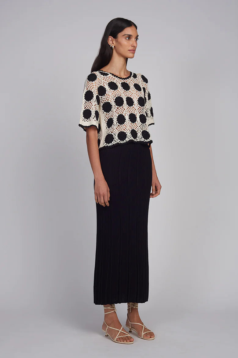 Woman wearing a polka dot top and black skirt on a gray background