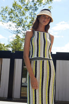Woman wearing a patterned dress and hat outdoors with trees and sky in the background