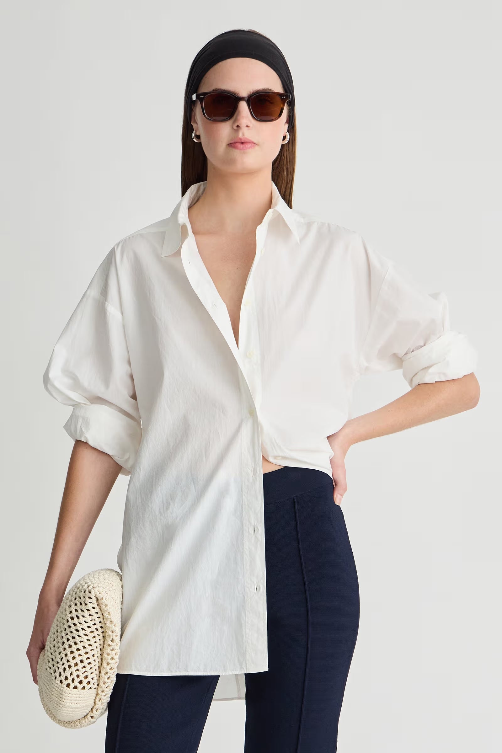 Woman wearing a white shirt and dark pants with sunglasses on a plain background