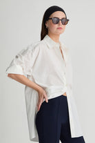 Woman wearing a white blouse and black pants against a plain background