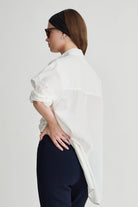 Woman wearing a white shirt and dark pants on a plain background