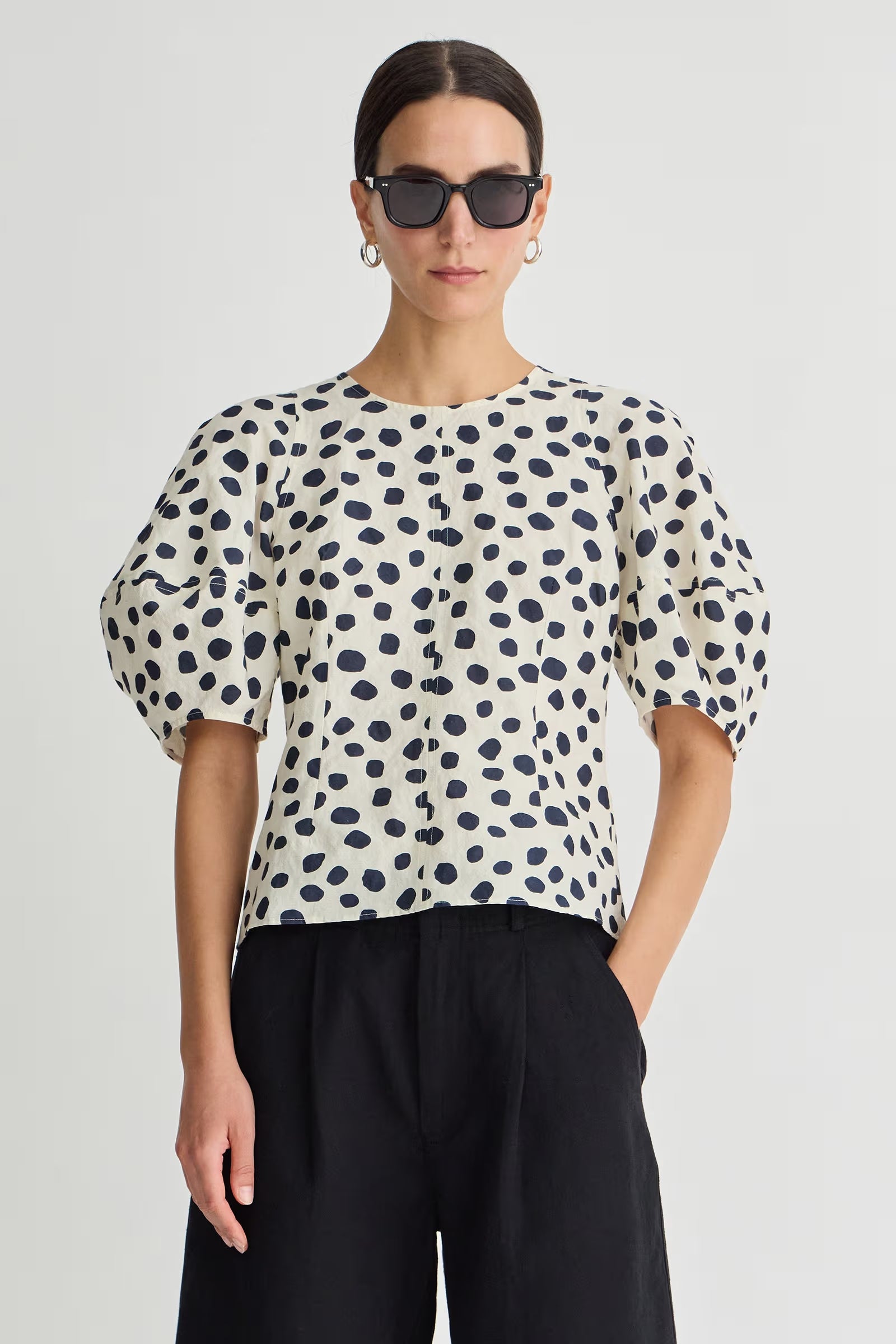 Woman wearing a polka dot blouse and sunglasses on a plain background