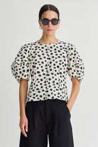 Woman wearing a polka dot blouse and sunglasses on a plain background