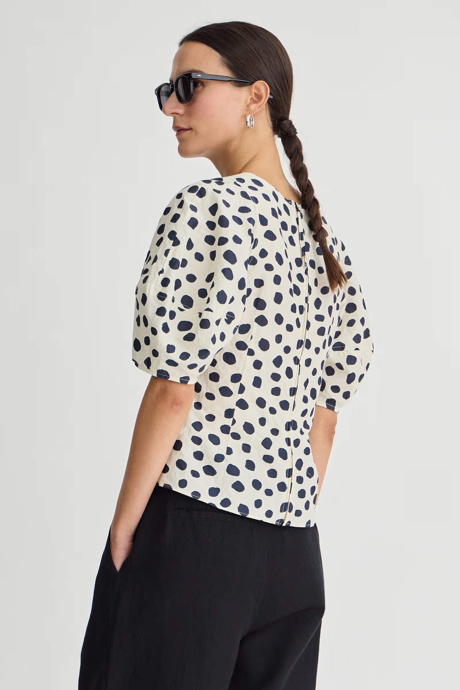 Woman wearing a polka dot blouse and sunglasses on a plain background