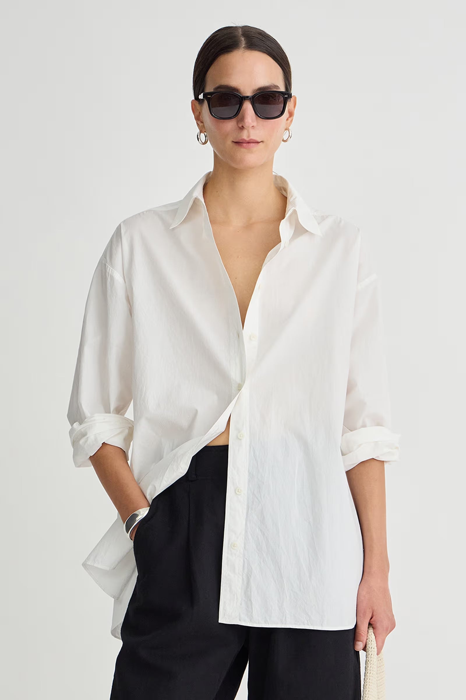 Person wearing a white oversized shirt and black pants on a plain background