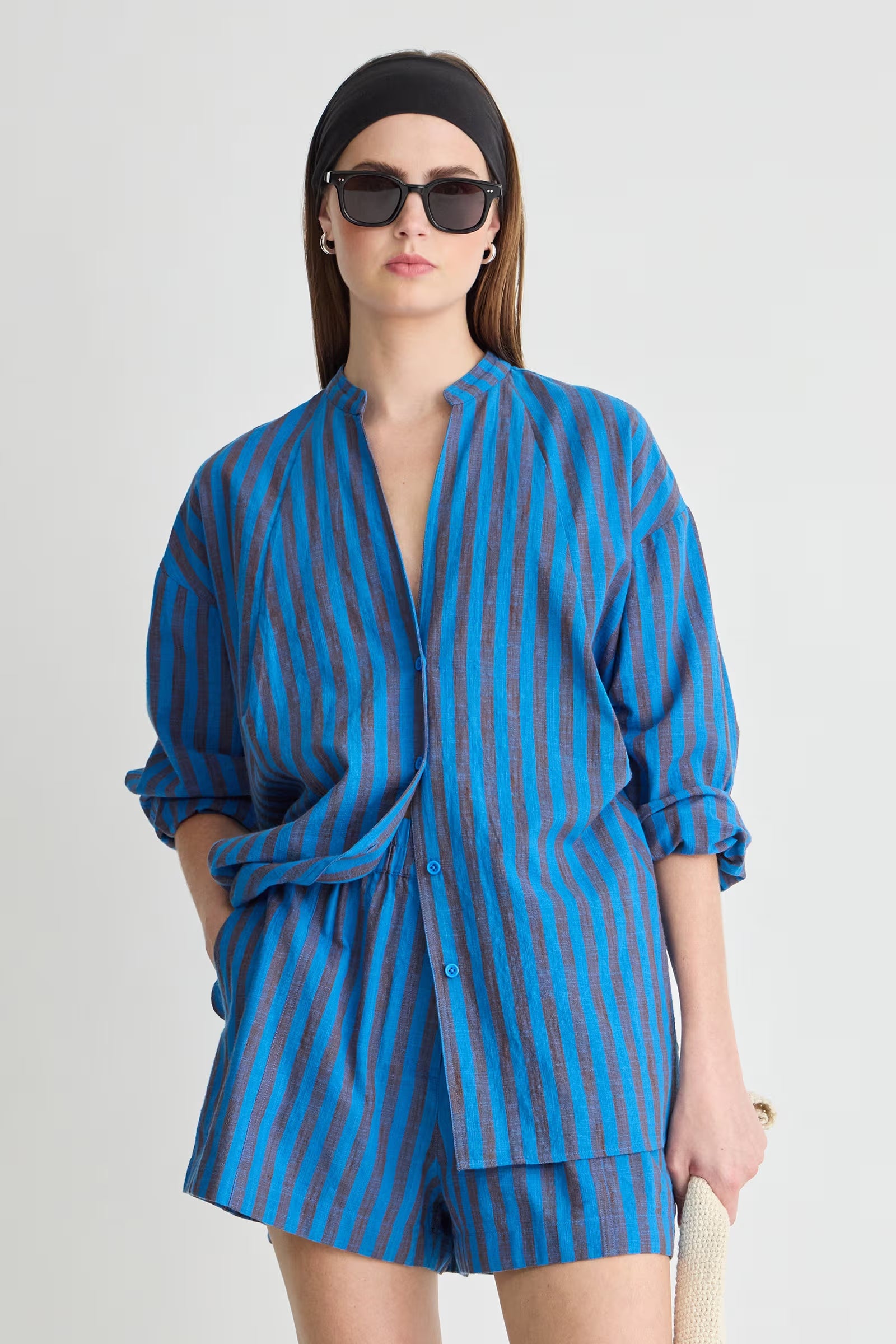 Woman wearing a blue striped outfit with sunglasses on a white background