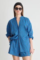 Woman wearing a blue striped outfit with sunglasses on a white background