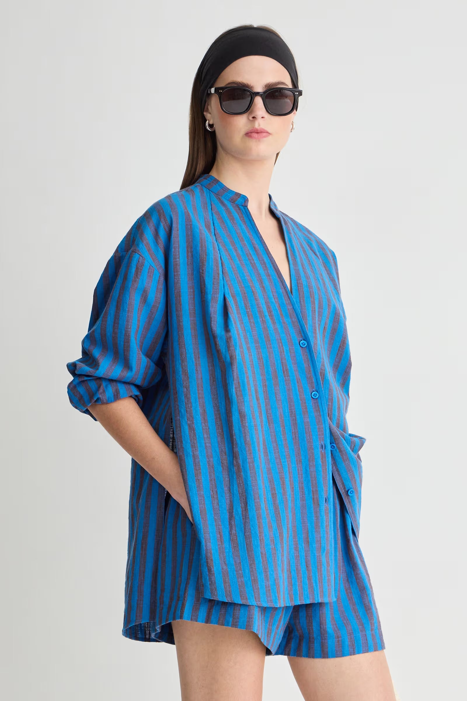 Woman wearing a blue striped outfit with a black headscarf and sunglasses on a white background