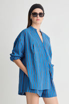 Woman wearing a blue striped outfit with a black headscarf and sunglasses on a white background