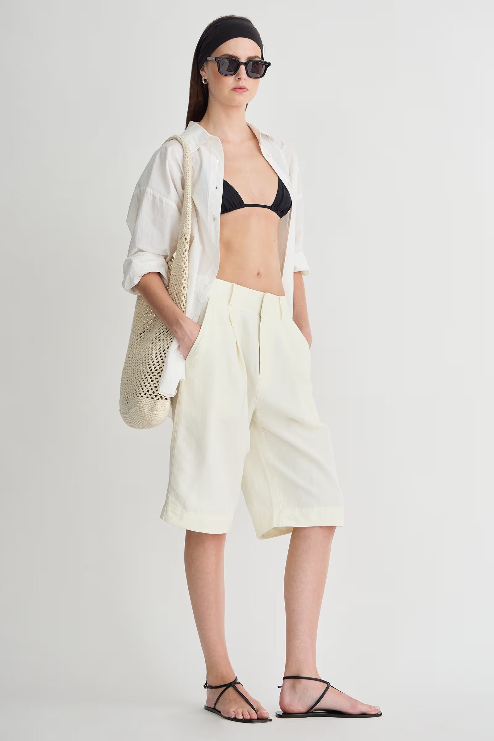 Woman wearing a black bikini top, white shorts, and a white jacket on a plain background
