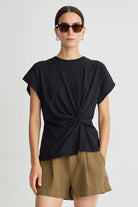 Woman wearing a black top with a knot detail and green shorts on a white background
