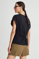 Woman wearing a black top with a knot detail and green shorts on a white background