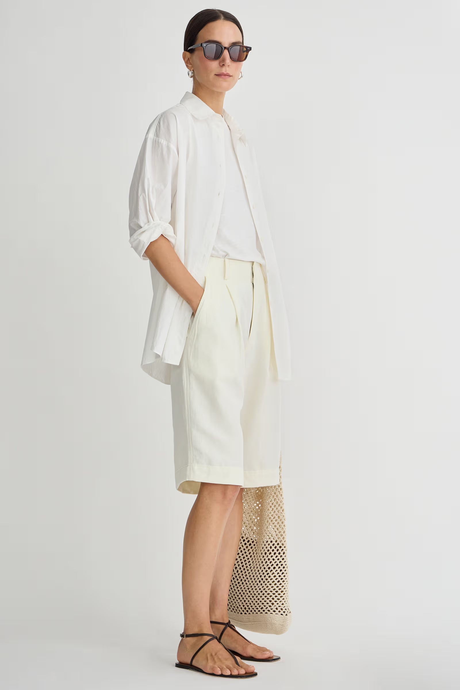 Woman wearing a white shirt and cream-colored pants on a plain background