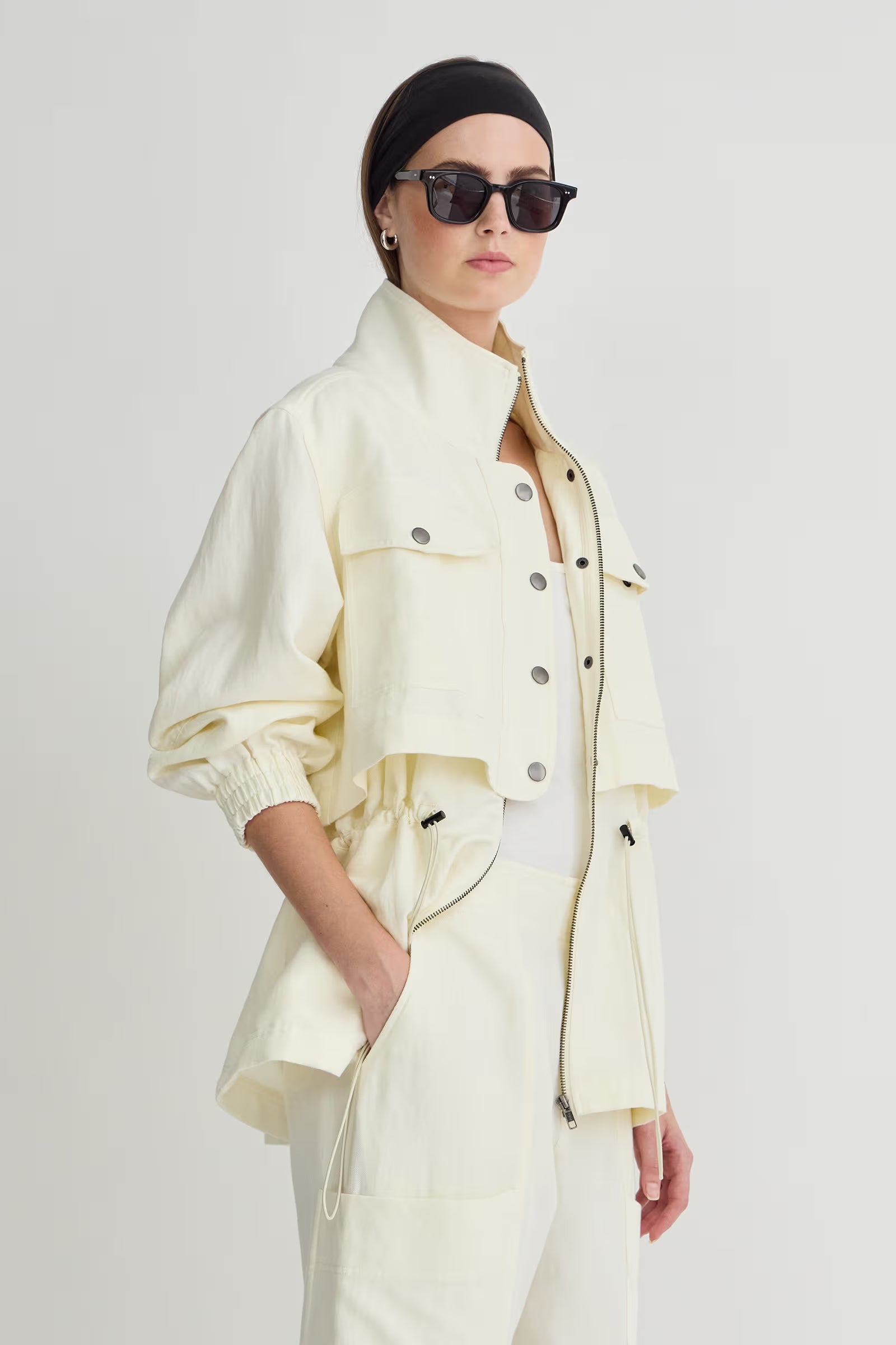 Woman wearing a cream-colored outfit with sunglasses on a white background