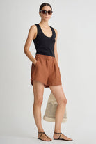 Woman wearing a black tank top and brown shorts on a white background