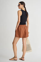 Woman wearing a black sleeveless top and brown skirt, holding a beige bag on a white background