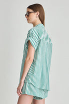 Woman wearing a green and white striped shirt and shorts on a light gray background