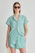 Woman wearing a green and white striped shirt and shorts set on a plain background