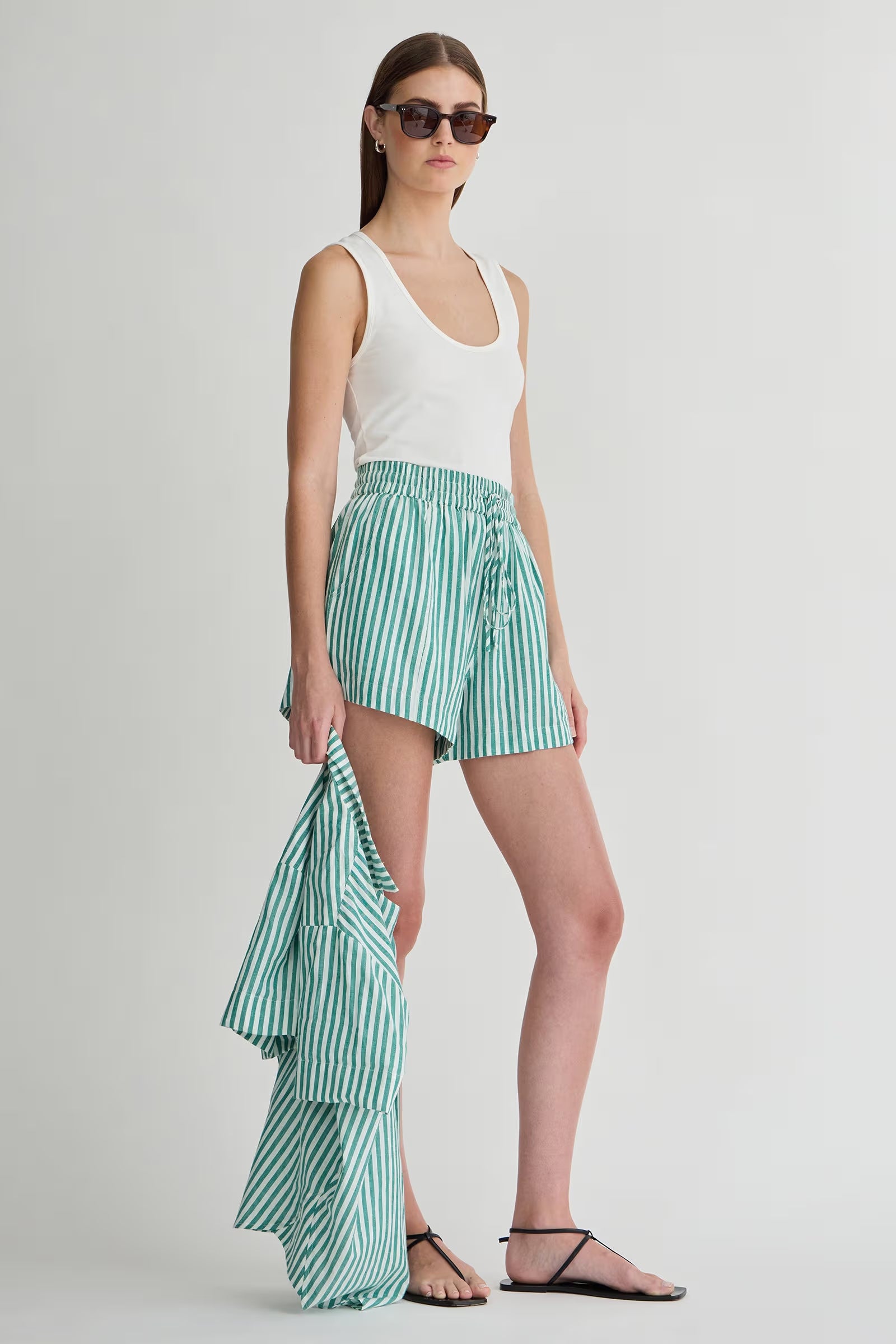 Woman wearing a white sleeveless top and green striped shorts on a plain background
