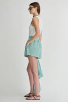 Woman wearing a white top and green striped skirt on a plain background