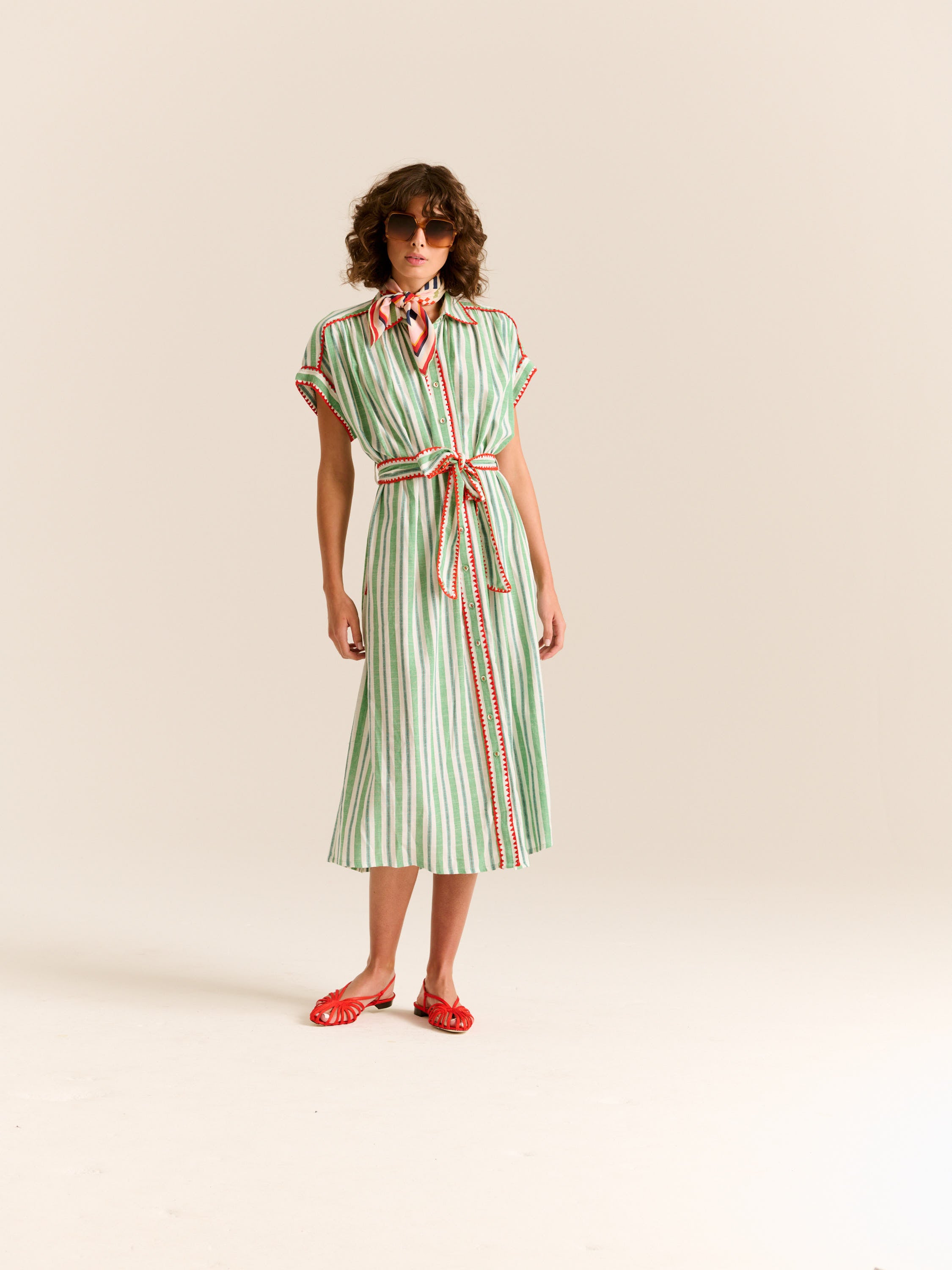 Woman wearing a green and white striped dress with a belt on a beige background