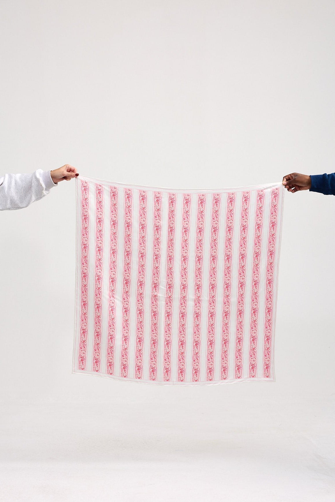 Two people holding a pink and white patterned fabric against a white background