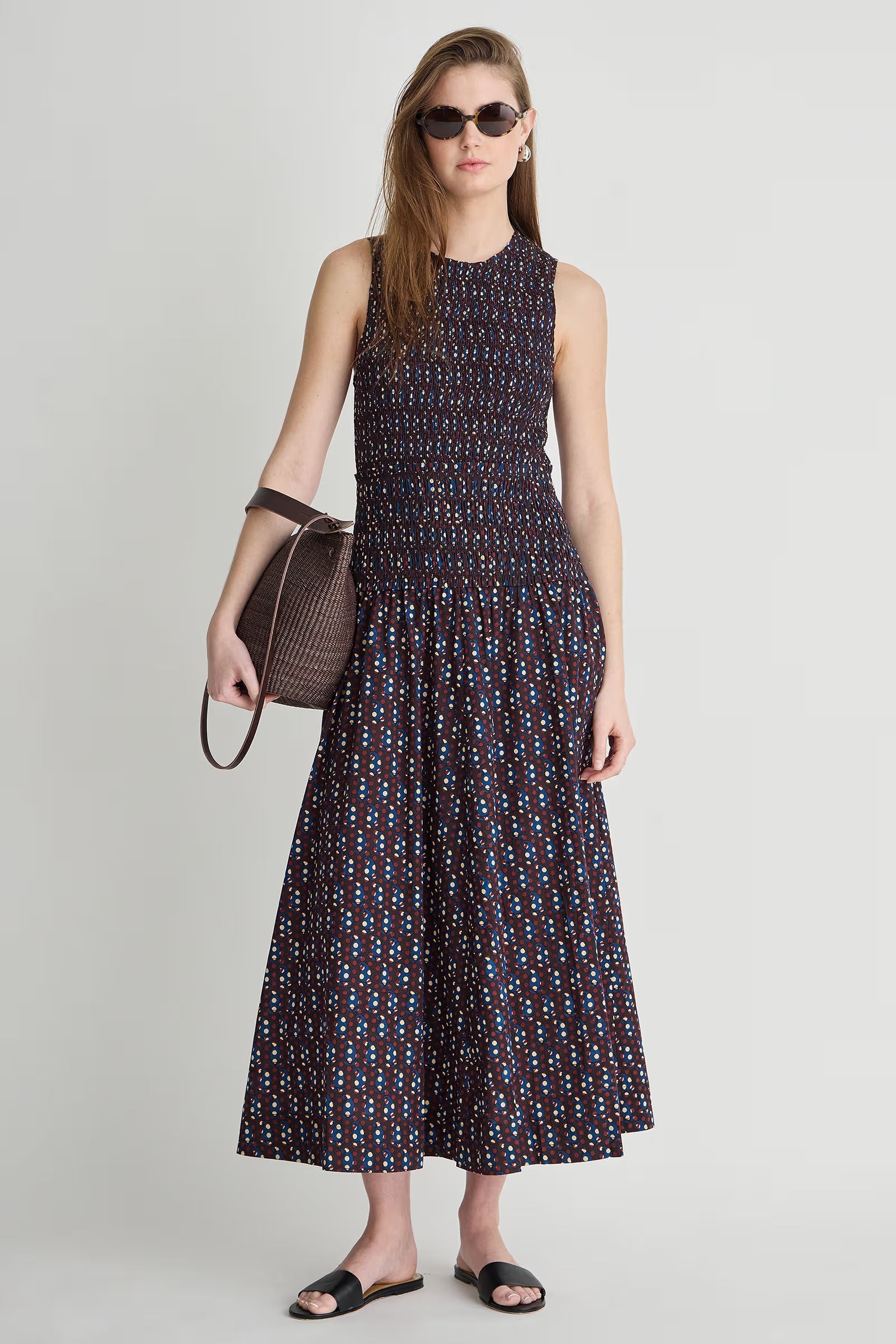 Woman wearing a patterned dress holding a handbag on a plain background