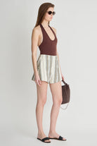 Woman wearing a brown halter top and striped shorts, holding a brown handbag on a white background