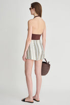 Woman wearing a strapless top and striped skirt with a woven bag on a plain background