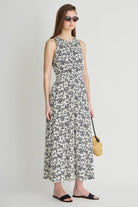 Woman wearing a floral dress holding a yellow bag on a plain background