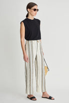 Woman wearing a black sleeveless top and striped pants on a white background