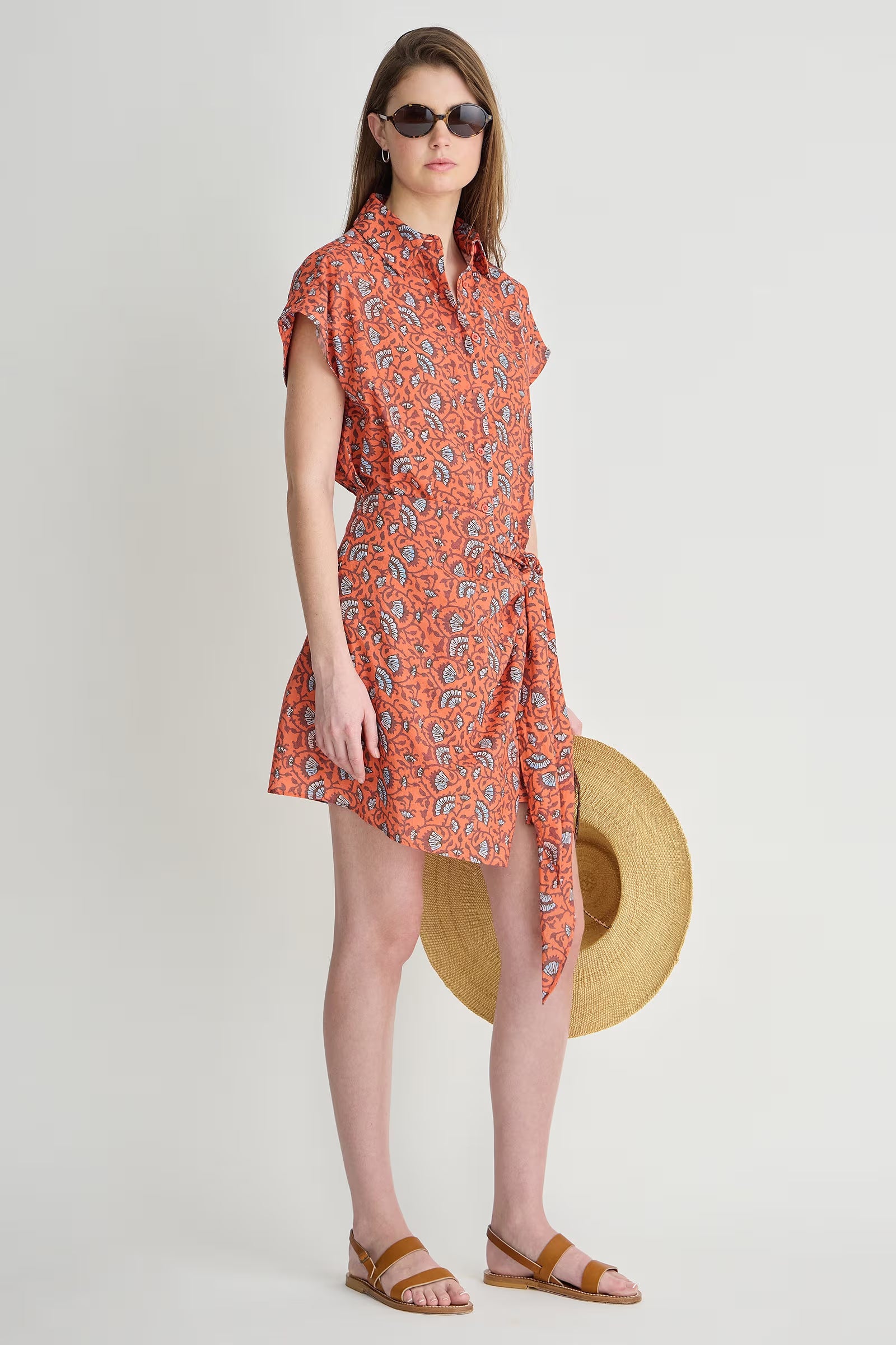 Woman wearing an orange patterned dress with a straw hat on a white background