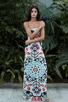 Woman wearing a strapless dress with a colorful pattern standing in front of green foliage.
