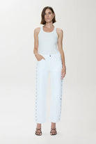 Woman wearing a white sleeveless top and light blue jeans on a white background