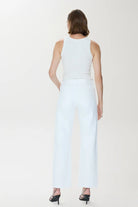 Woman wearing a sleeveless top and light blue pants on a white background