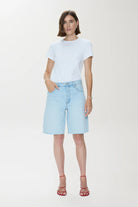 Woman wearing a light blue t-shirt and denim shorts on a white background