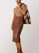 Person wearing a brown leather skirt with a beige top and plaid jacket on a white background