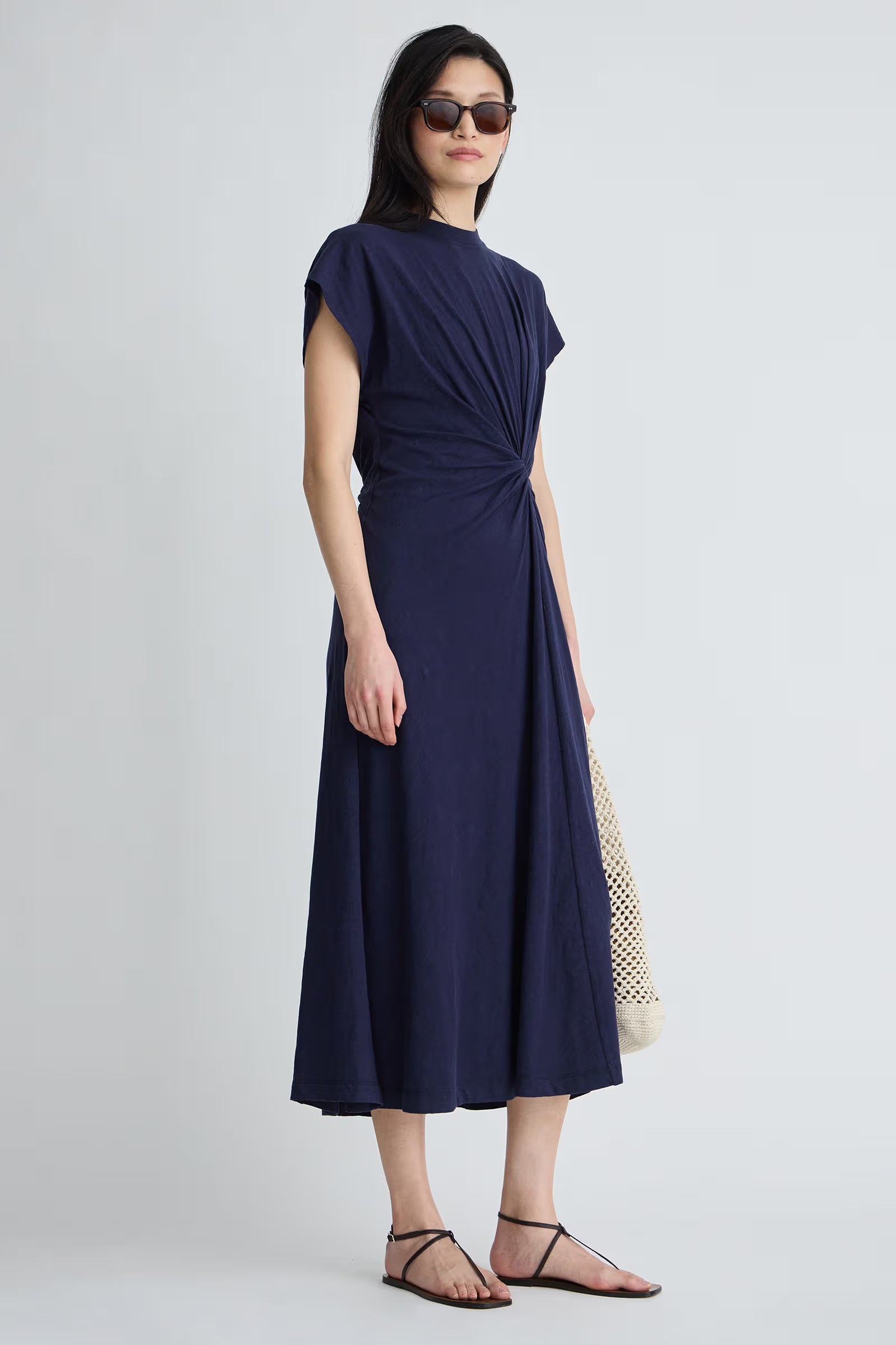 Woman wearing a navy blue dress with sunglasses on a white background