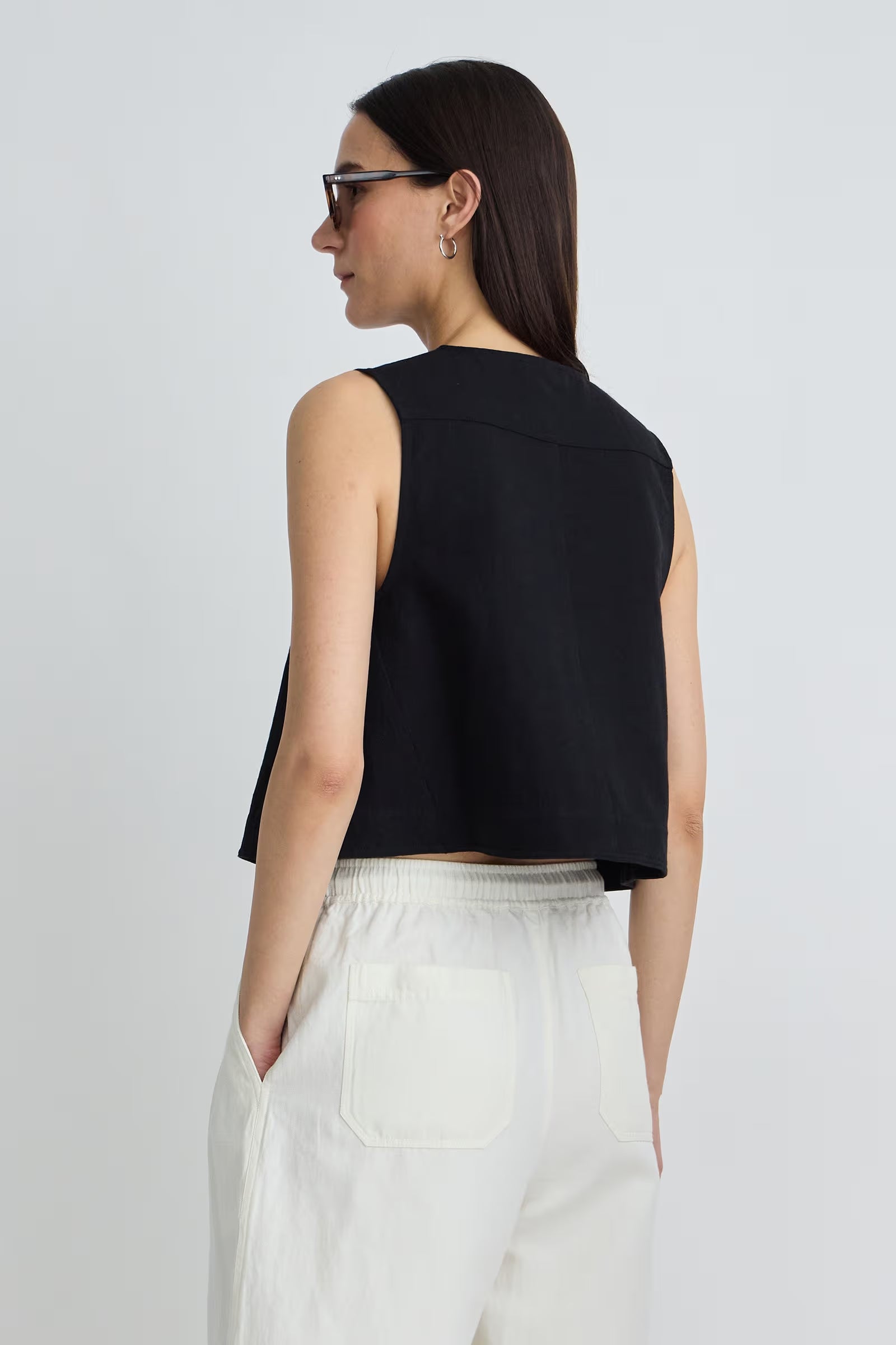 Woman wearing a black sleeveless top and white pants on a light gray background