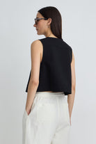 Woman wearing a black sleeveless top and white pants on a light gray background