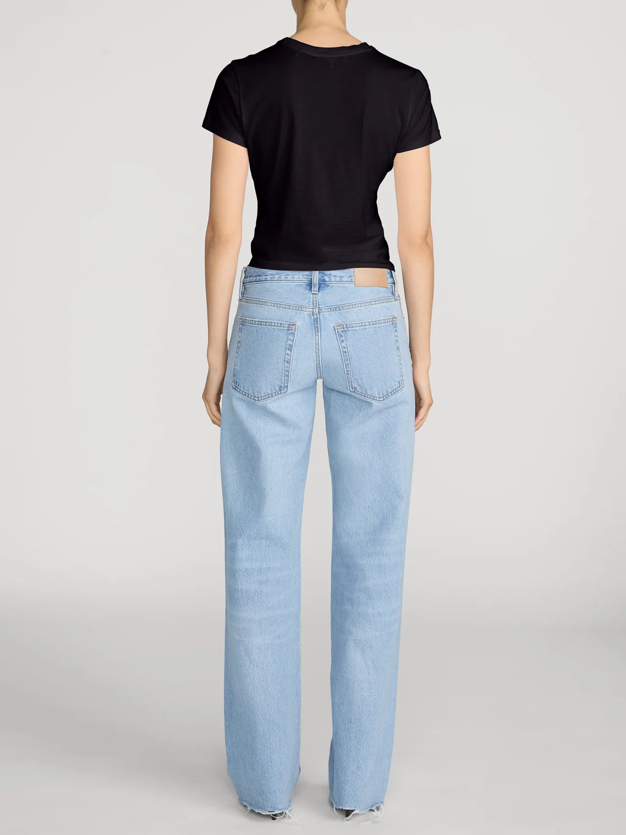 A model shown from the back wearing a black short-sleeve t-shirt and light-wash blue straight-leg jeans against a light gray studio background.