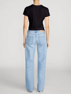 A model shown from the back wearing a black short-sleeve t-shirt and light-wash blue straight-leg jeans against a light gray studio background.
